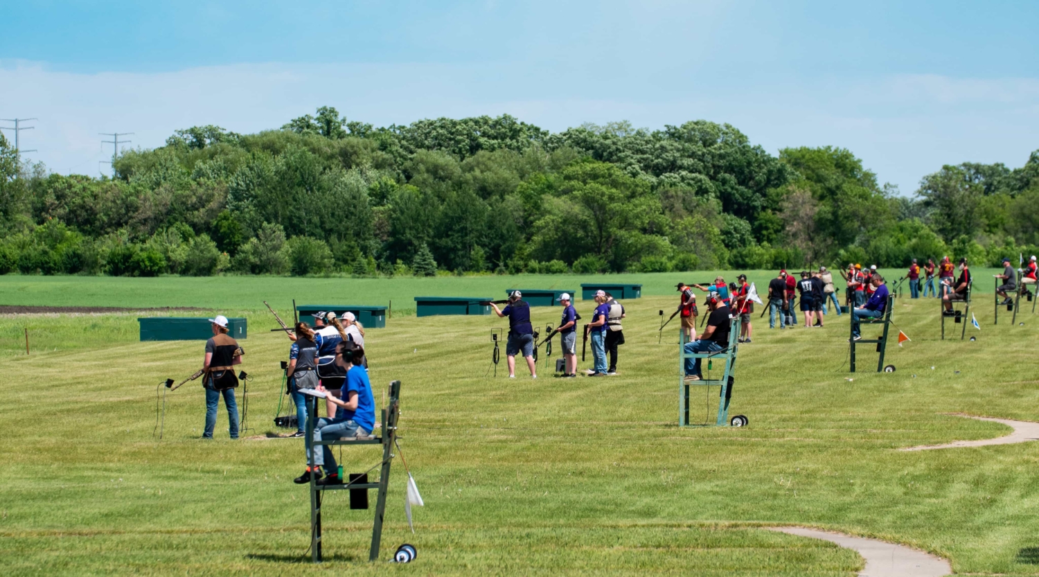 A group of people standing in a shooting range ready to shoot.