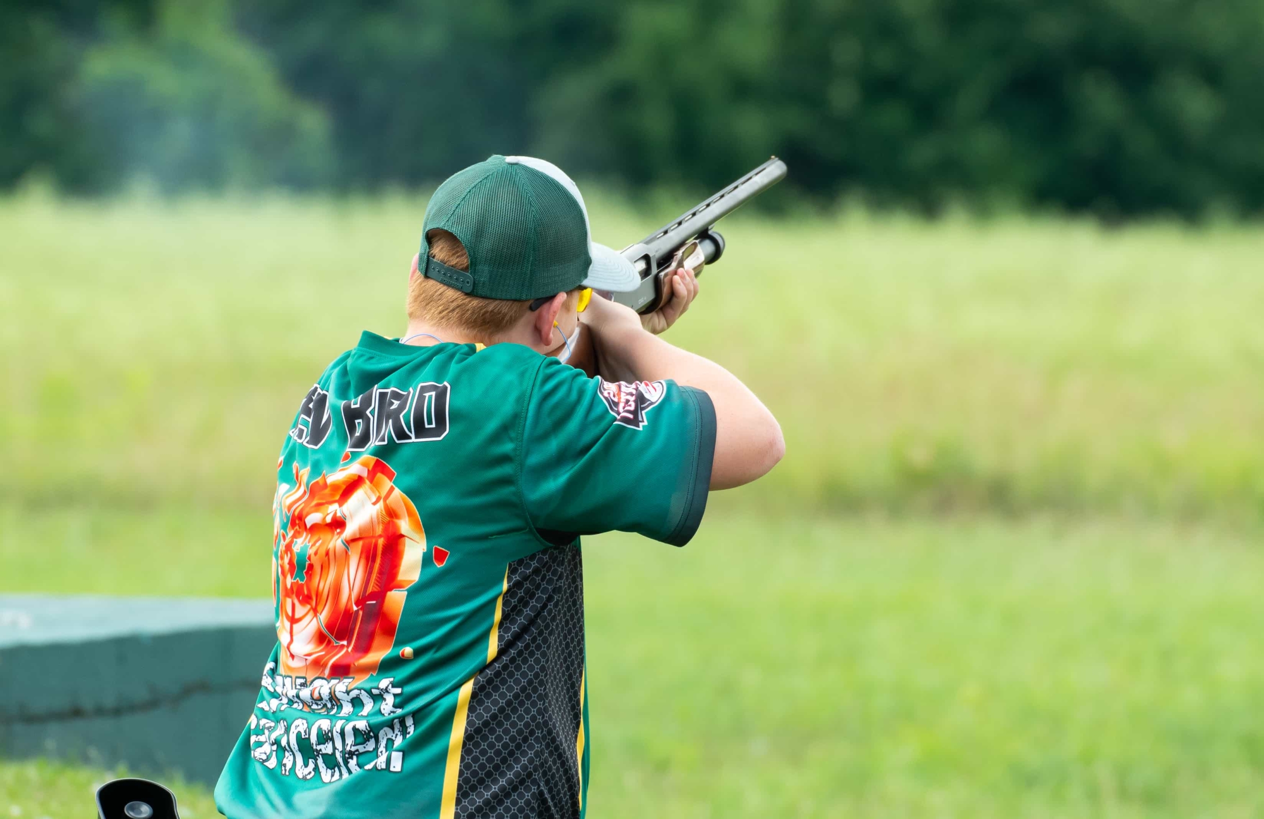 A young man shooting a gun in a field.